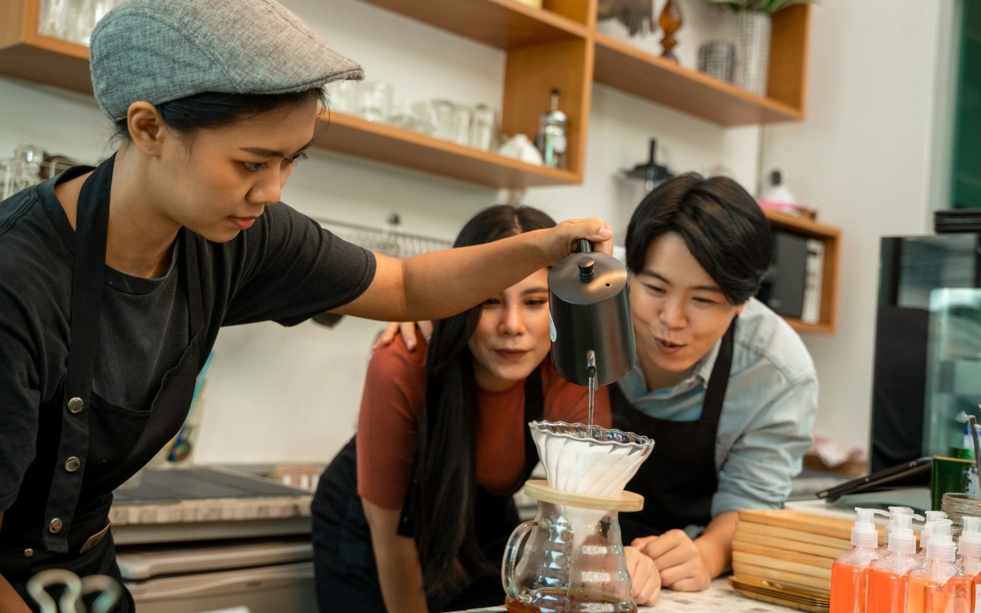 barista-pouring-boiling-water-from-kettle-to-drip-coffee-maker-at-the-bar-of-the-modern-cafe--e1651630662286